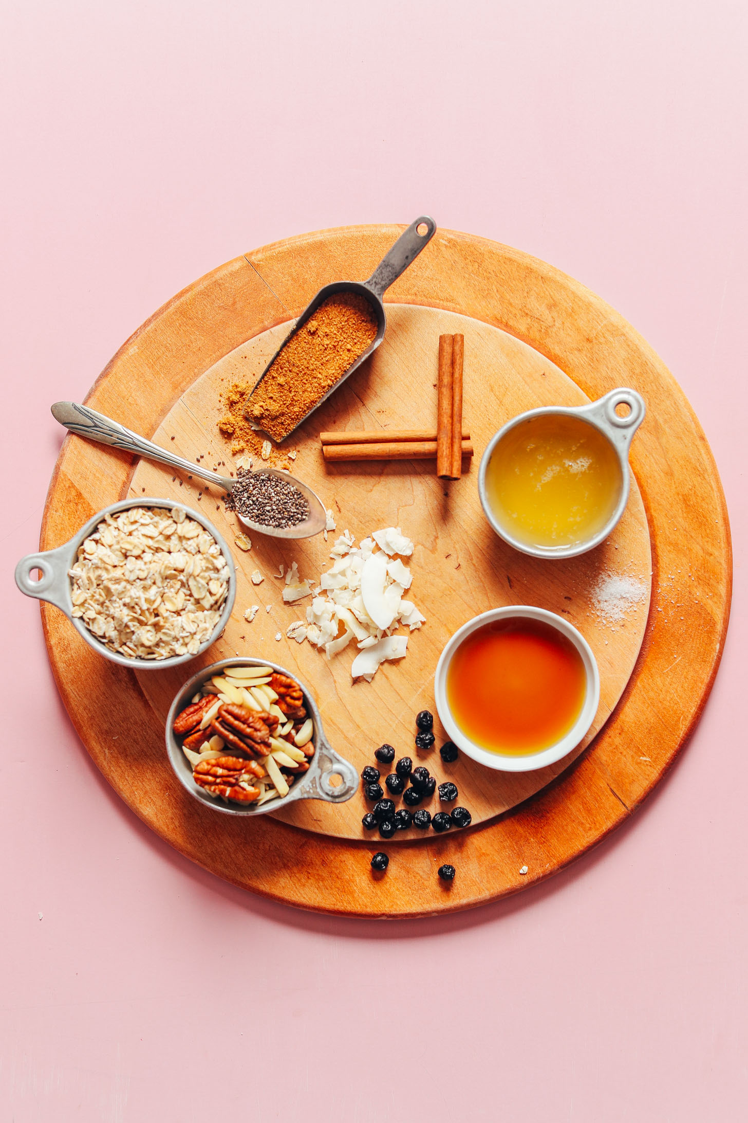 Cutting board with oats, pecans, almonds, dried blueberries, maple syrup, cinnamon, coconut, and chia seeds for our vegan gluten-free granola recipe