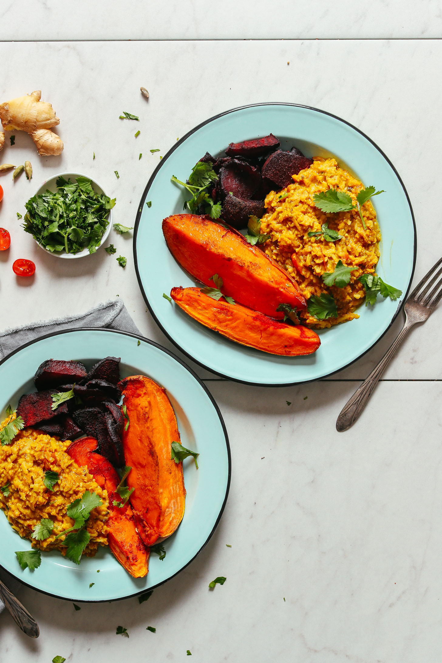Two plates filled with roasted sweet potato and beets alongside Cauliflower Rice Kitchari for a comforting plant-based meal