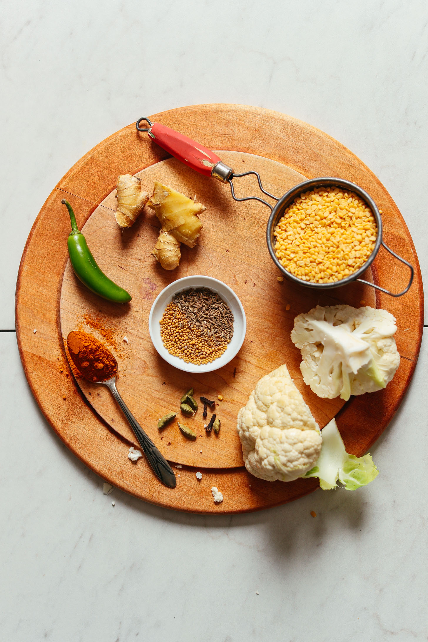 Wood cutting board showcasing ginger, serrano, cauliflower, and moong dal for making Cauliflower Rice Kitchari