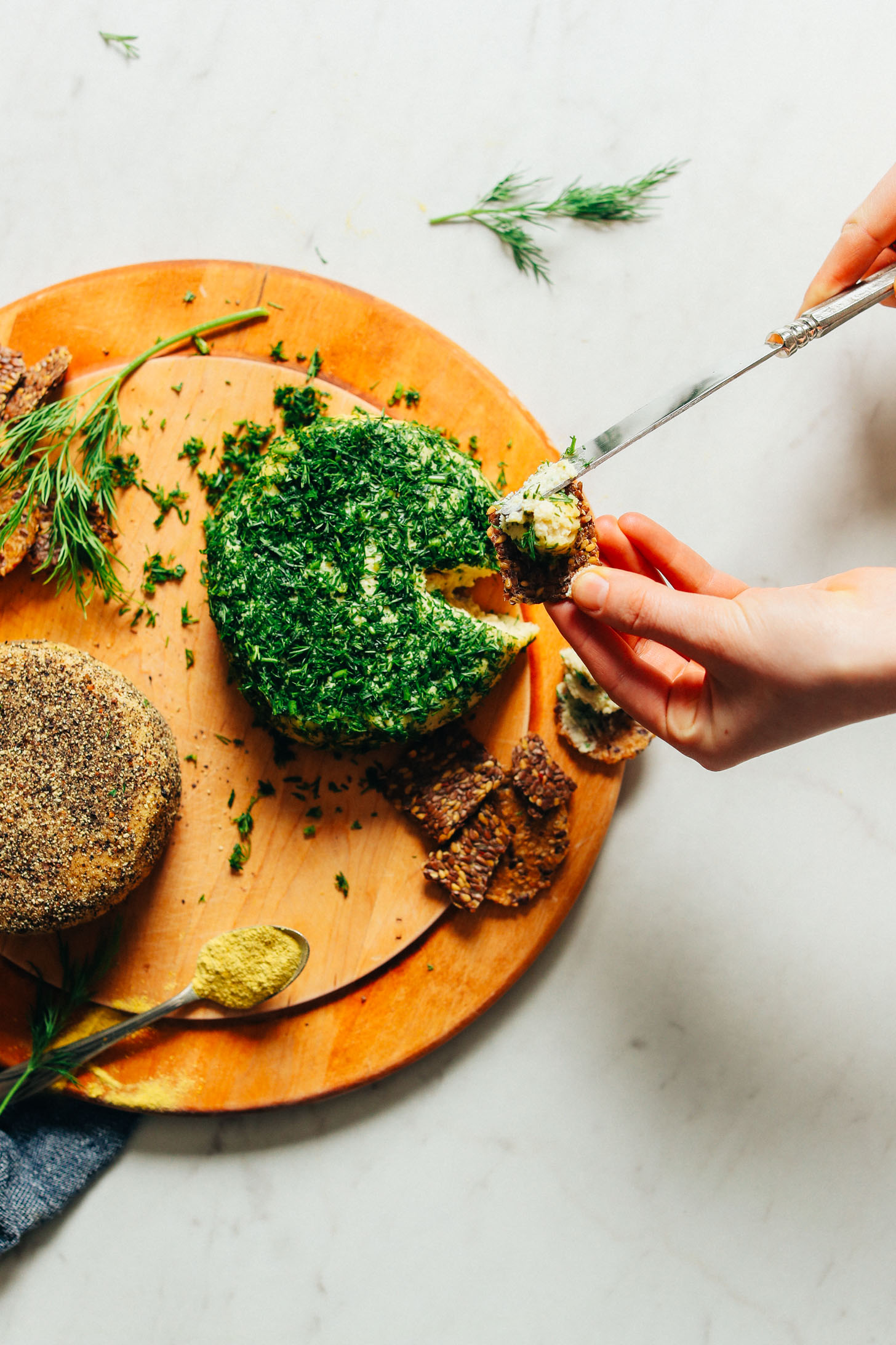 Using a knife to spread homemade vegan cheese onto a cracker for a plant-based snack