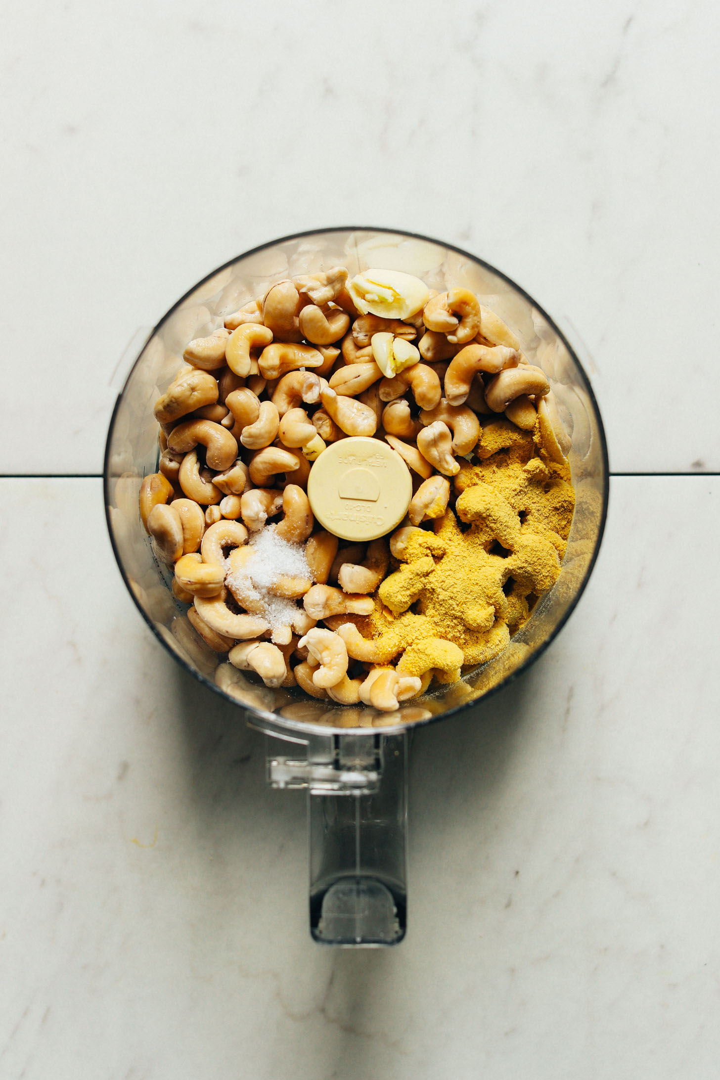 Food processor filled with cashews, nutritional yeast, salt, and garlic for making homemade plant-based cheese