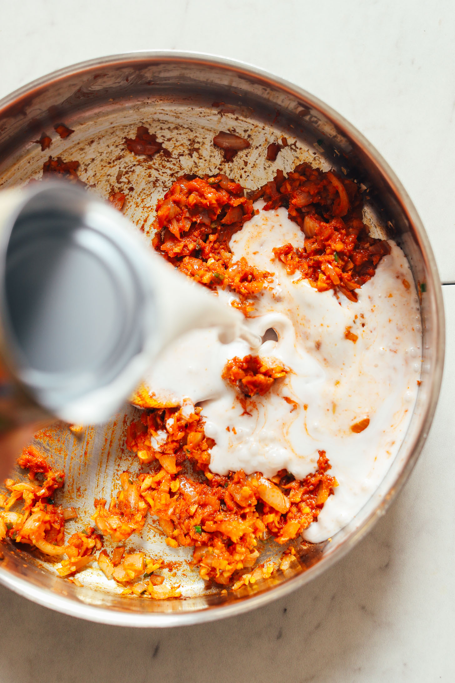 Pouring coconut milk into onion and spices mixture for 1-Pot Yellow Chickpea Cauliflower Curry
