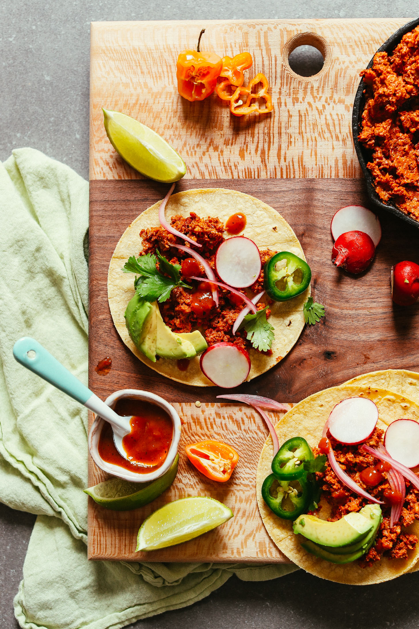 Wood cutting board with corn tortillas topped with Vegan Taco "Meat", radishes, avocado, and jalapenos