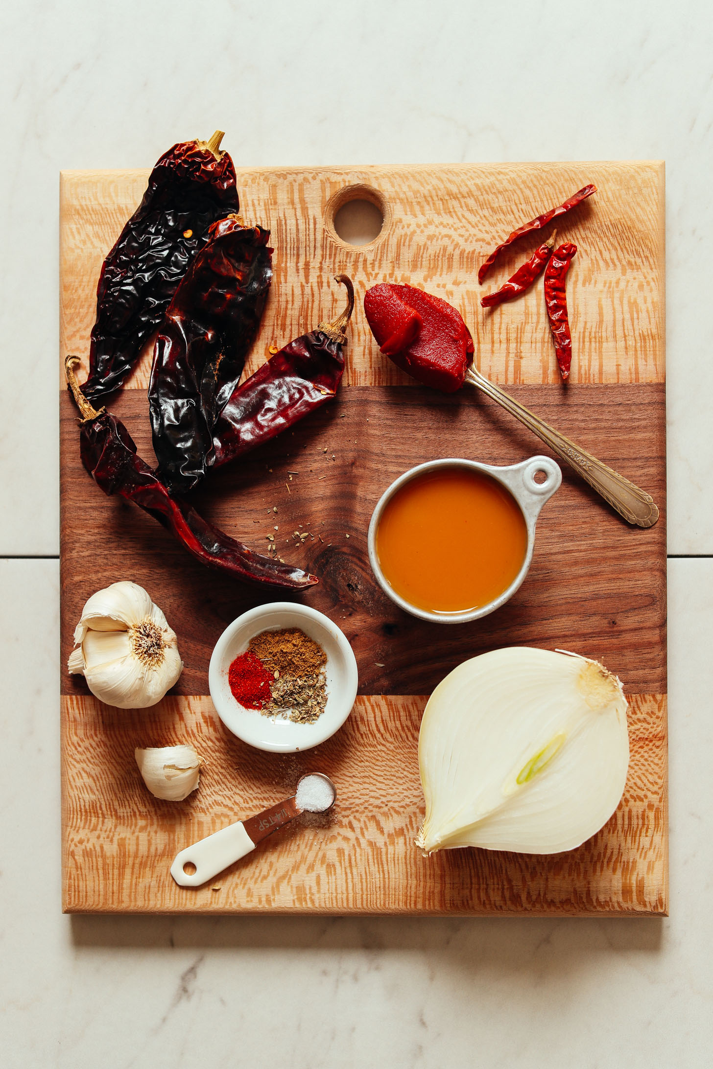 Cutting board with onion, garlic, chilies, vegetables broth, tomato paste, salt, and spices for making homemade red enchilada sauce