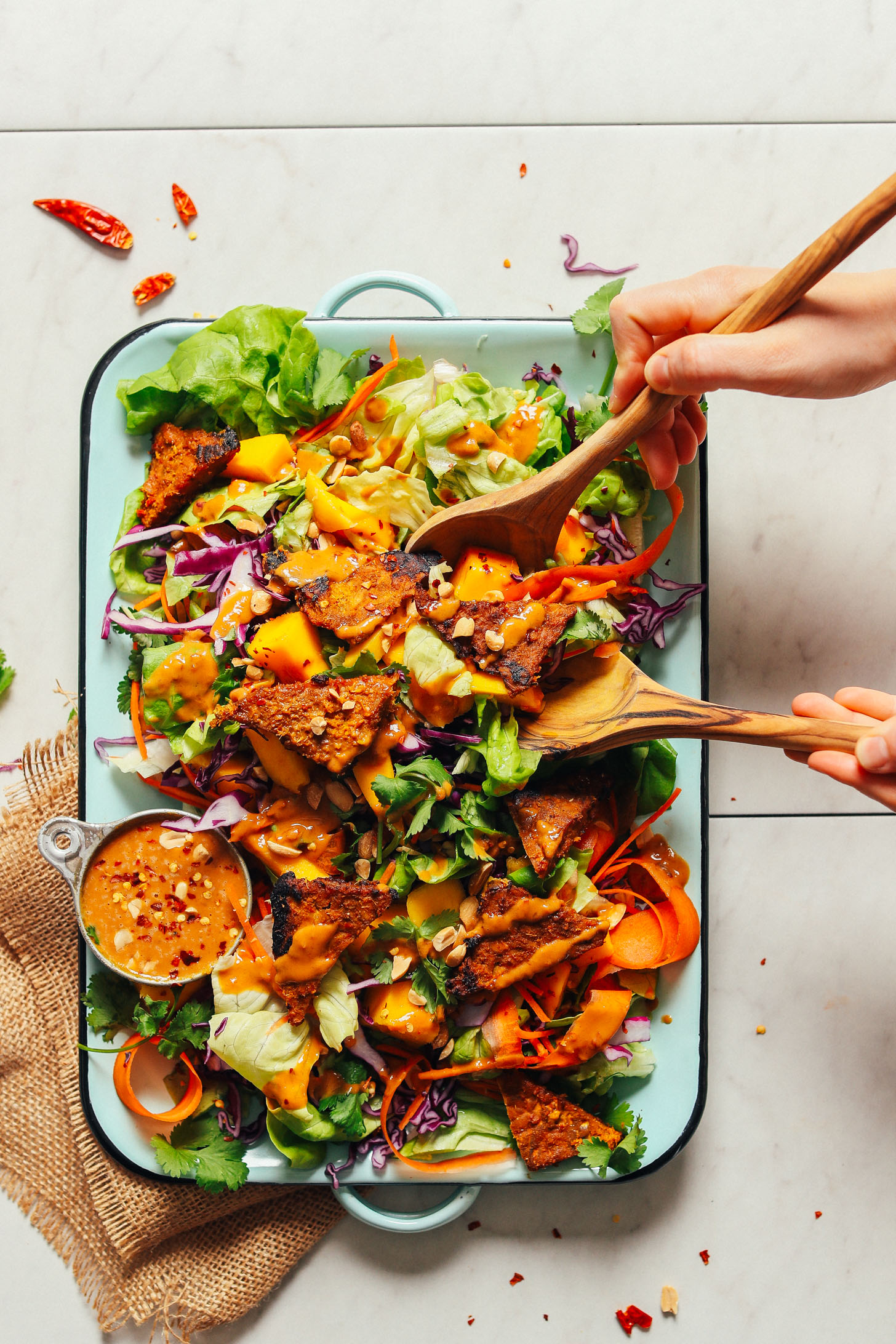 Using salad tongs to grab a serving of Healthy Mango Green Salad with Creamy Peanut Dressing