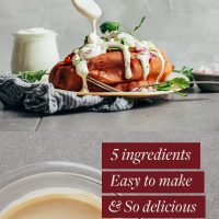 Using a small spoon to stir a bowl of Vegan Sour Cream and drizzle it on a roasted sweet potato