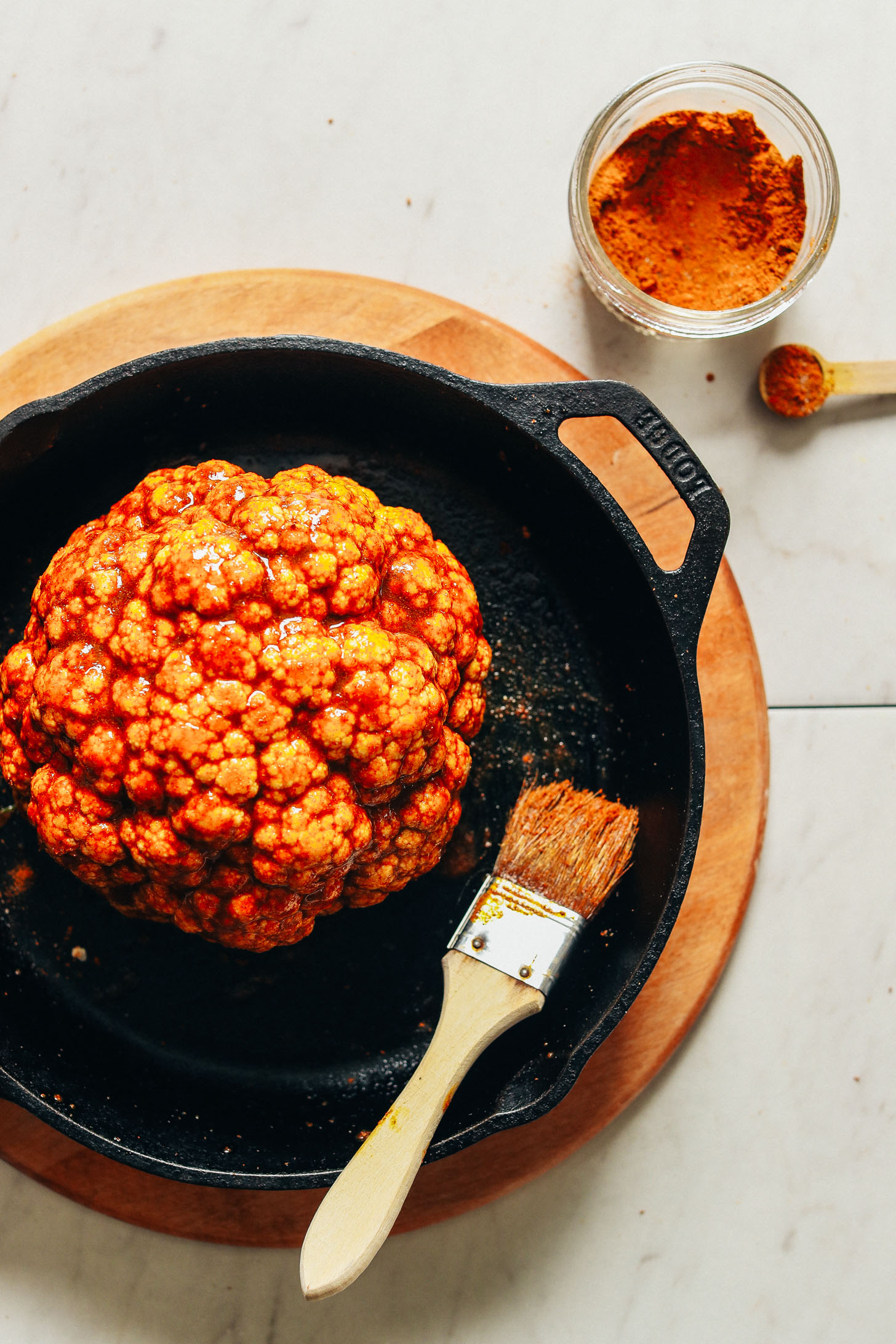 Using a pastry brush to spread oil and spice mixture onto head of cauliflower