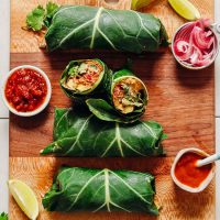 Cutting board with several Raw Burritos, lime wedges, and bowls of hot sauce, pickled onion, and salsa