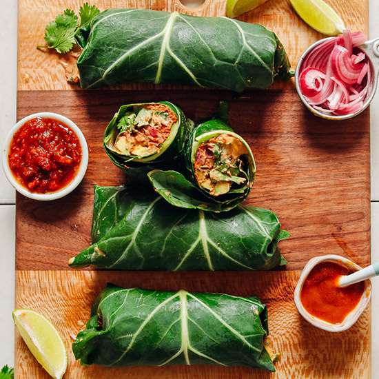 Cutting board with several Raw Burritos, lime wedges, and bowls of hot sauce, pickled onion, and salsa