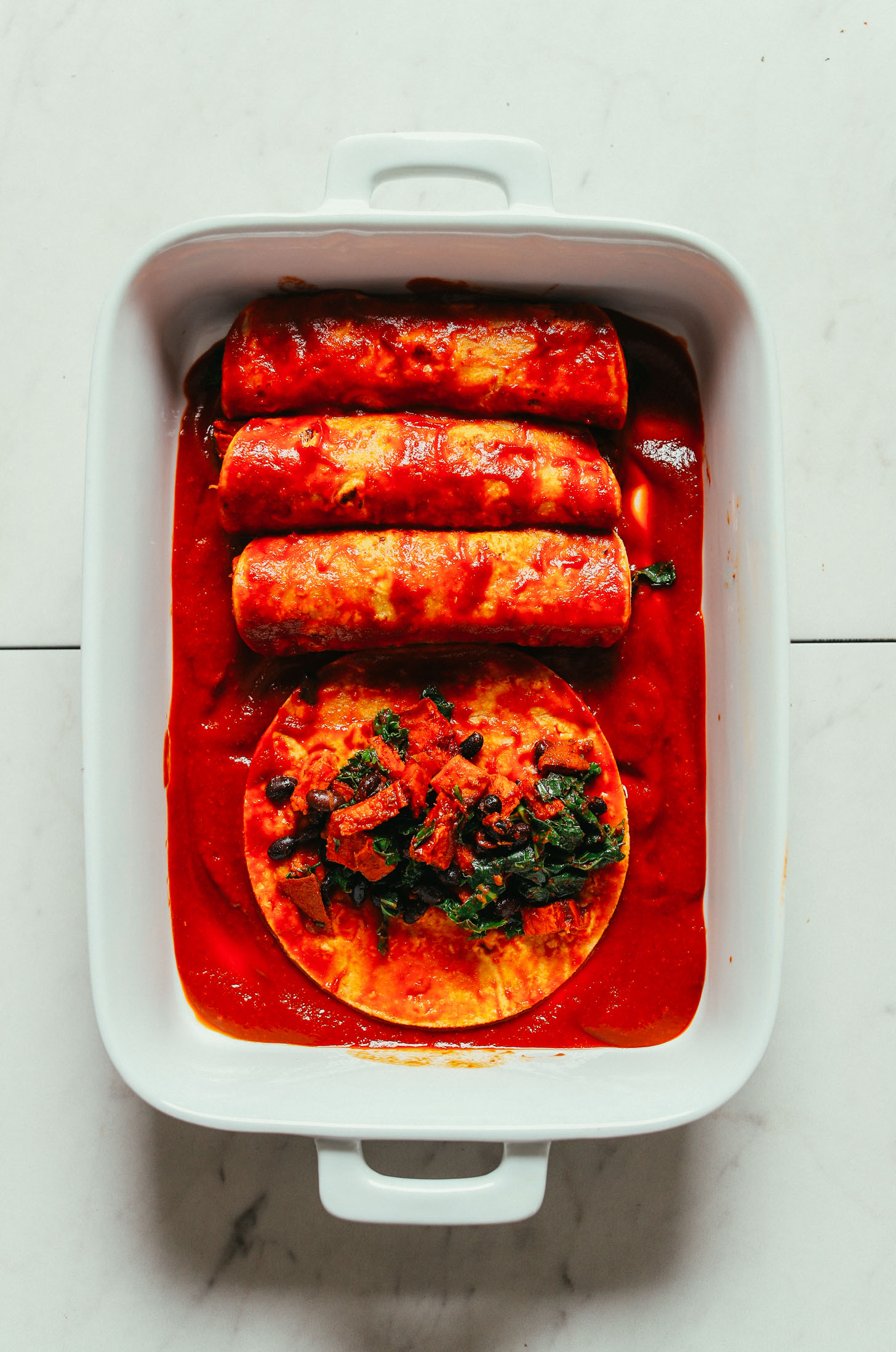Rolling up Sweet Potato Black Bean Enchiladas in homemade sauce in a baking dish