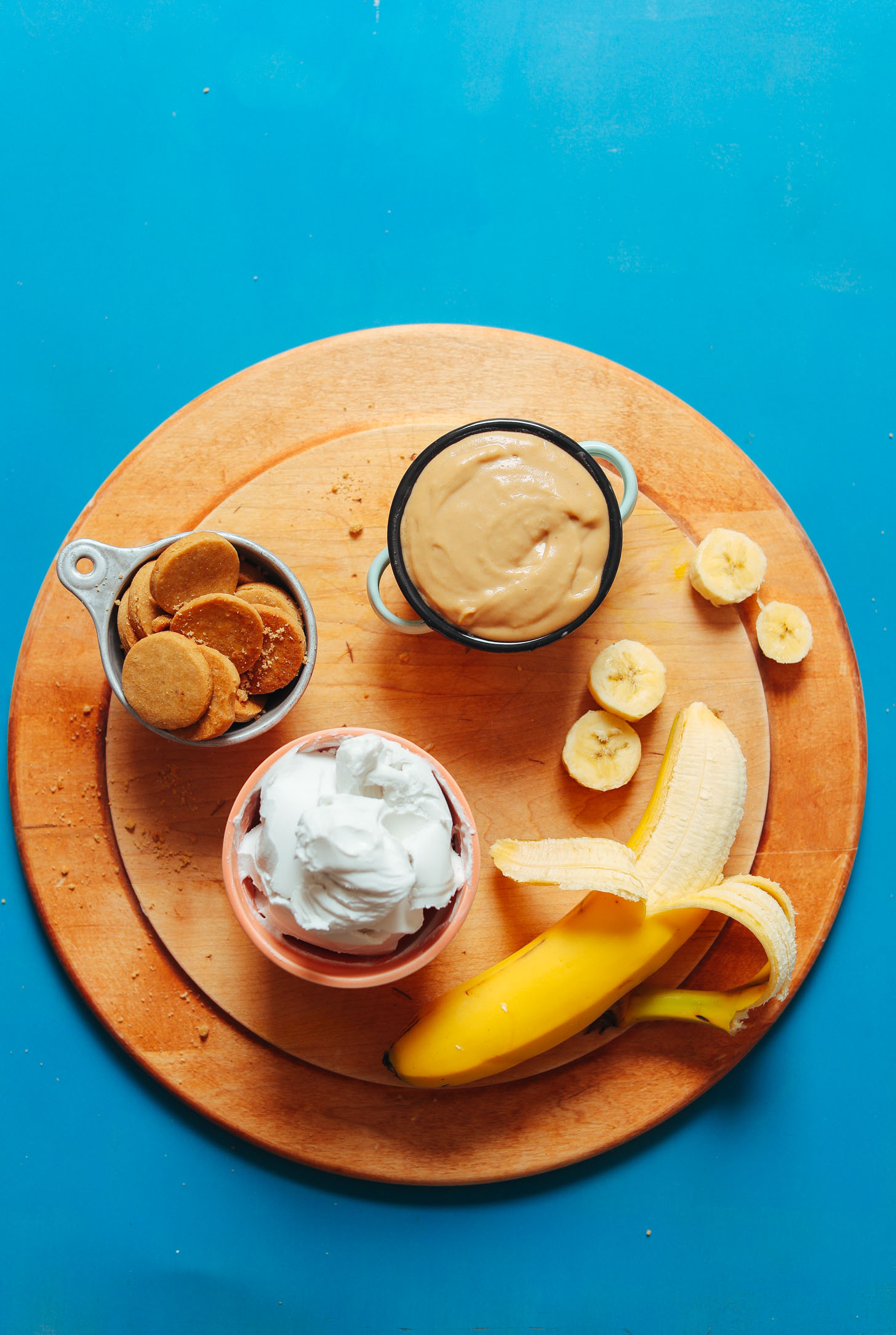 Cutting board with banana, coconut whip, peanut butter pudding, and vanilla wafers for a delicious gluten-free vegan dessert
