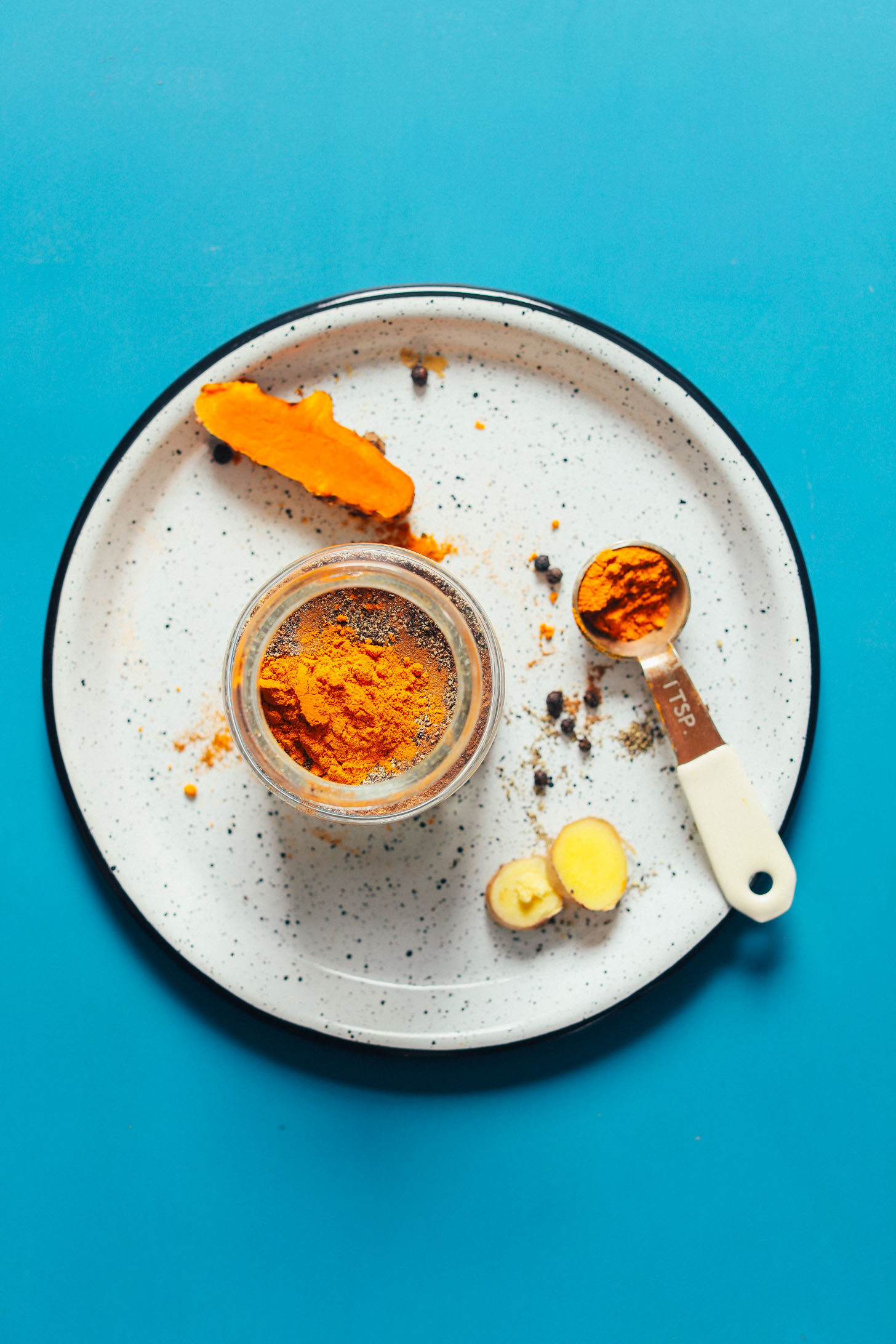 Jar and plate of spices for making perfect vegan golden milk