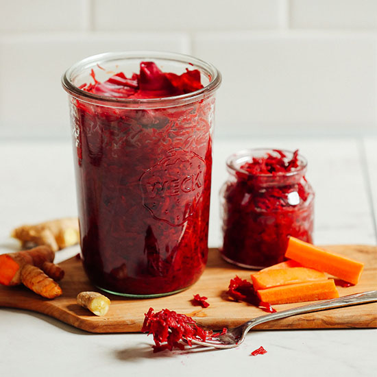 Cutting board with fresh ginger, turmeric, carrots, and jars of our homemade sauerkraut recipe