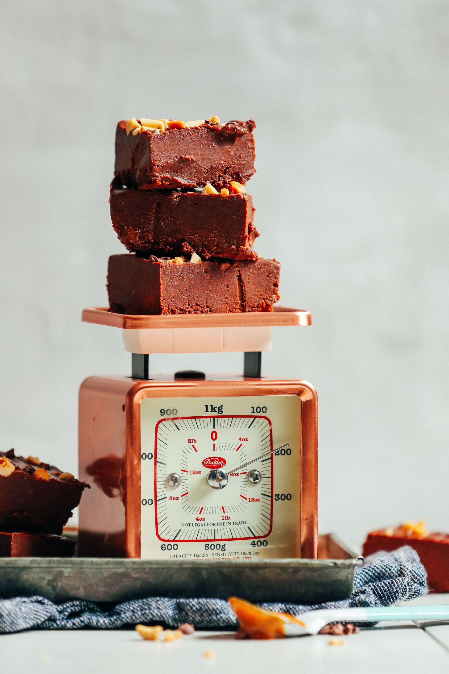 Squares of our 4-Ingredient Vegan Chocolate Peanut Butter Fudge recipe stacked on a vintage scale