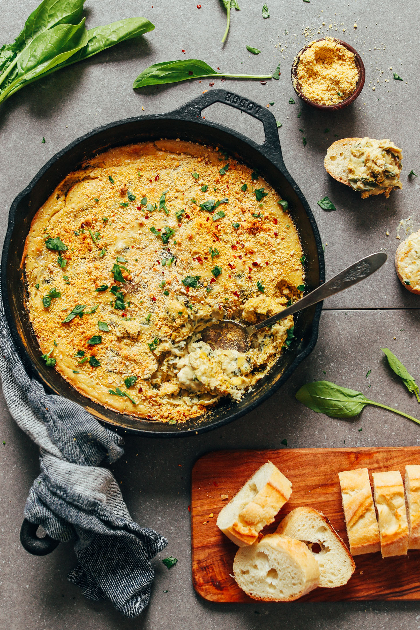 Spoon submerged in a skillet of homemade vegan GF Spinach Artichoke Dip