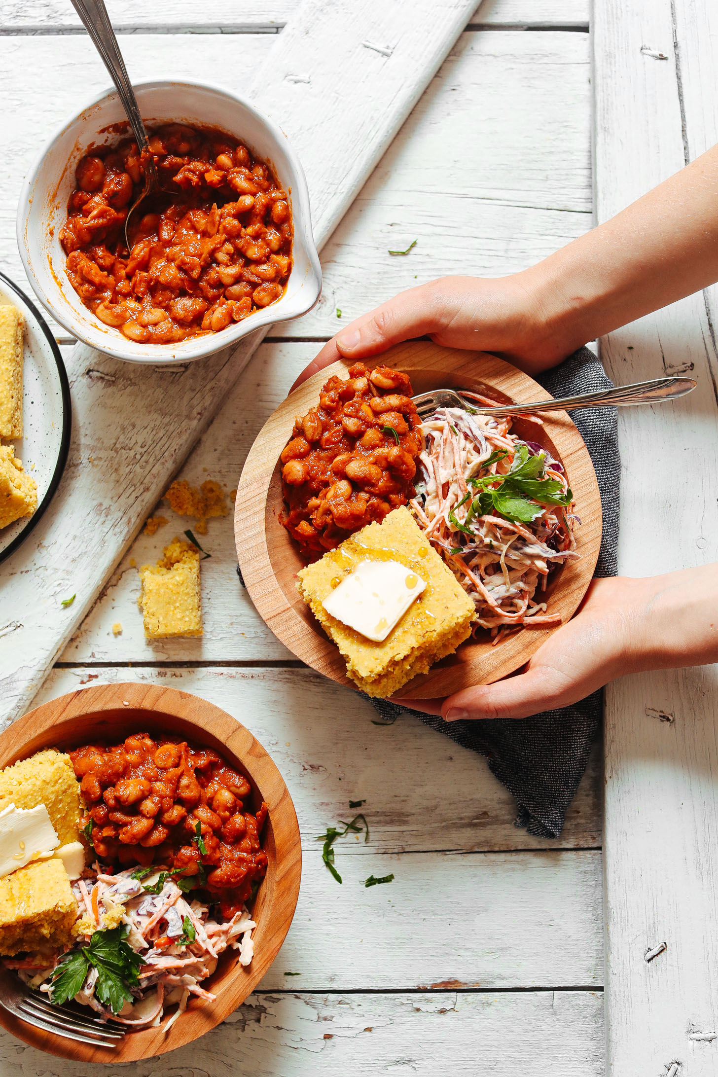 Holding out a bowl filled with Baked Beans, Coleslaw, and Cornbread for a GF vegan meal