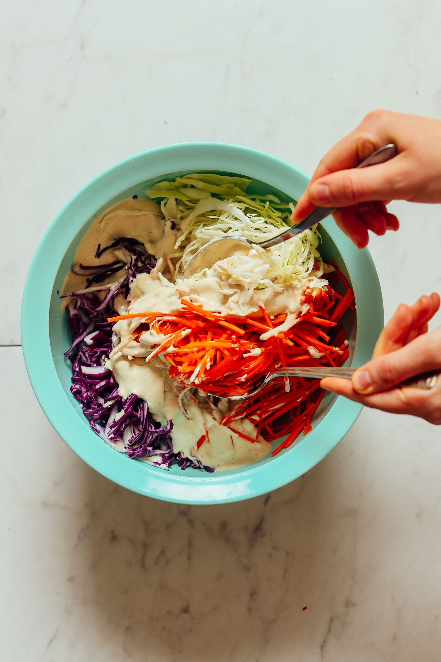 Using serving spoons to toss together vegetables and dressing for vegan coleslaw
