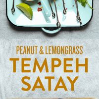 Baking sheet and blue tray holding a batch of our Lemongrass Tempeh skewers alongside a dish of peanut sauce