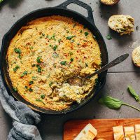 Using a spoon to grab a serving of Creamy Vegan Spinach and Artichoke Dip