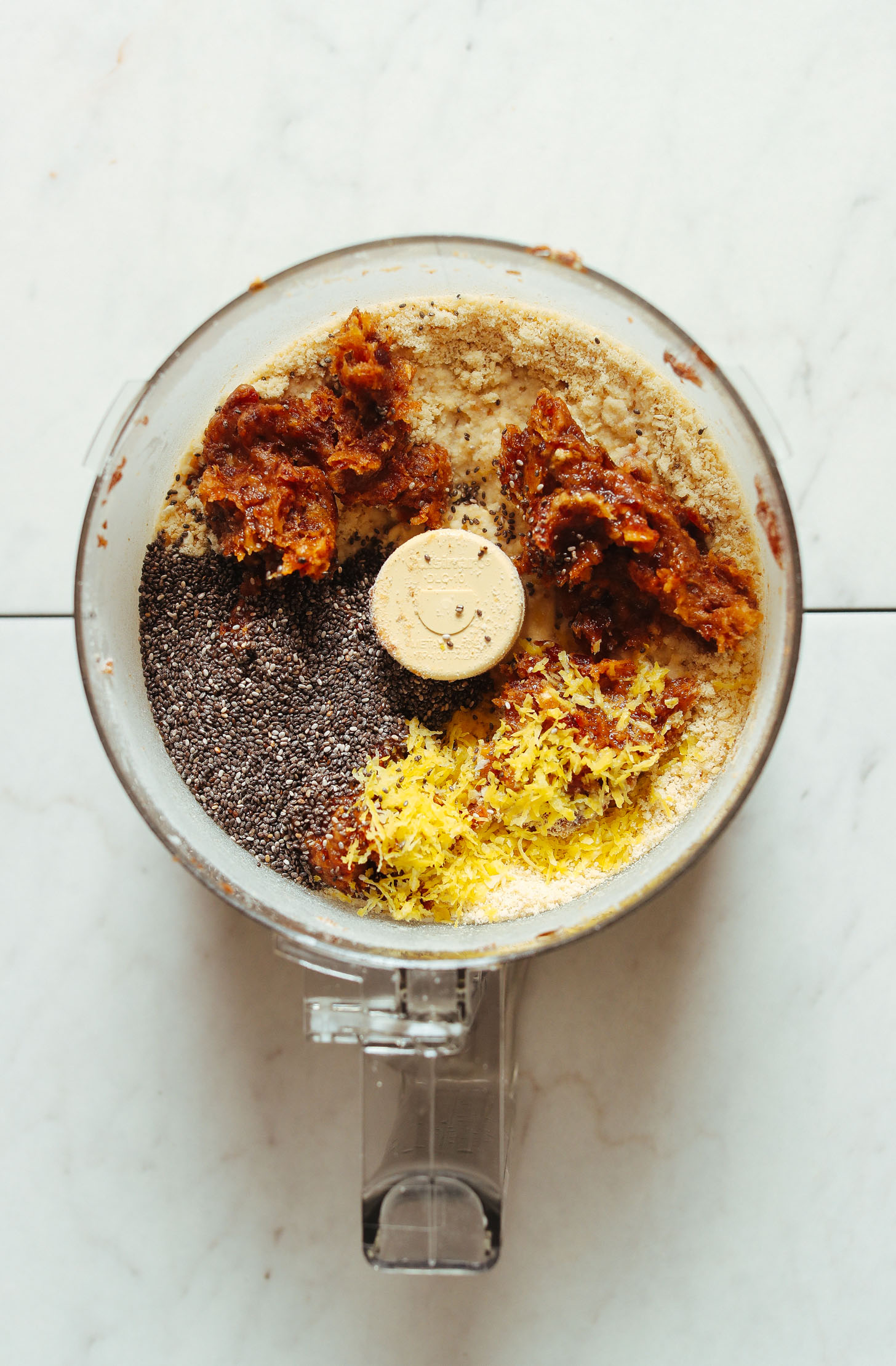 Food processor filled with ingredients for making gluten-free Vegan Lemon Poppyseed Donut Holes