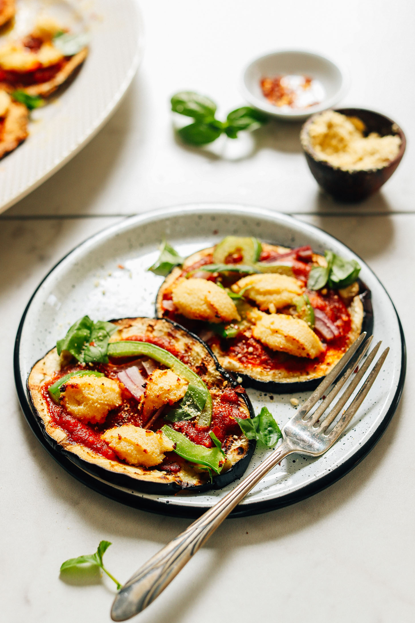 Plate of Mini Eggplant Pizzas topped with green onions, vegan ricotta, red onion, and more