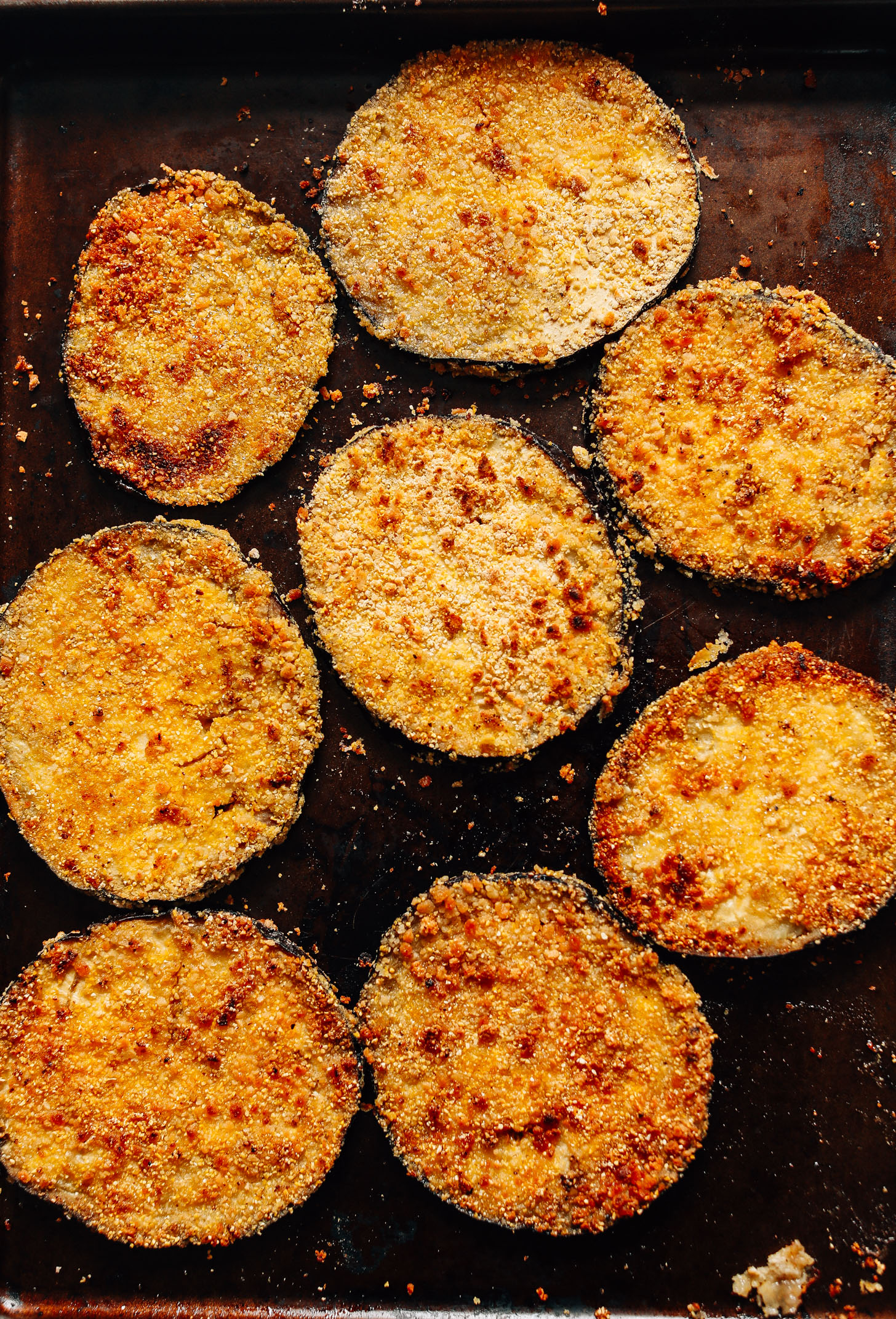 Baking sheet filled with crispy eggplant slices for Mini Eggplant Pizzas