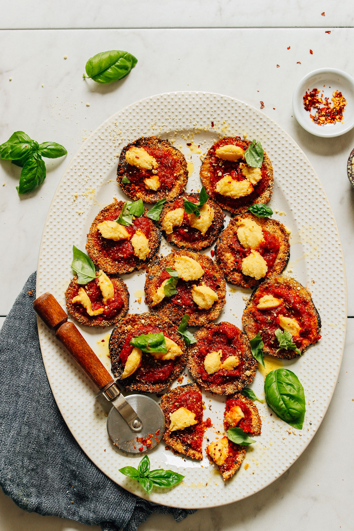 Platter of Mini Eggplant Pizzas topped with vegan macadamia ricotta and fresh basil leaves