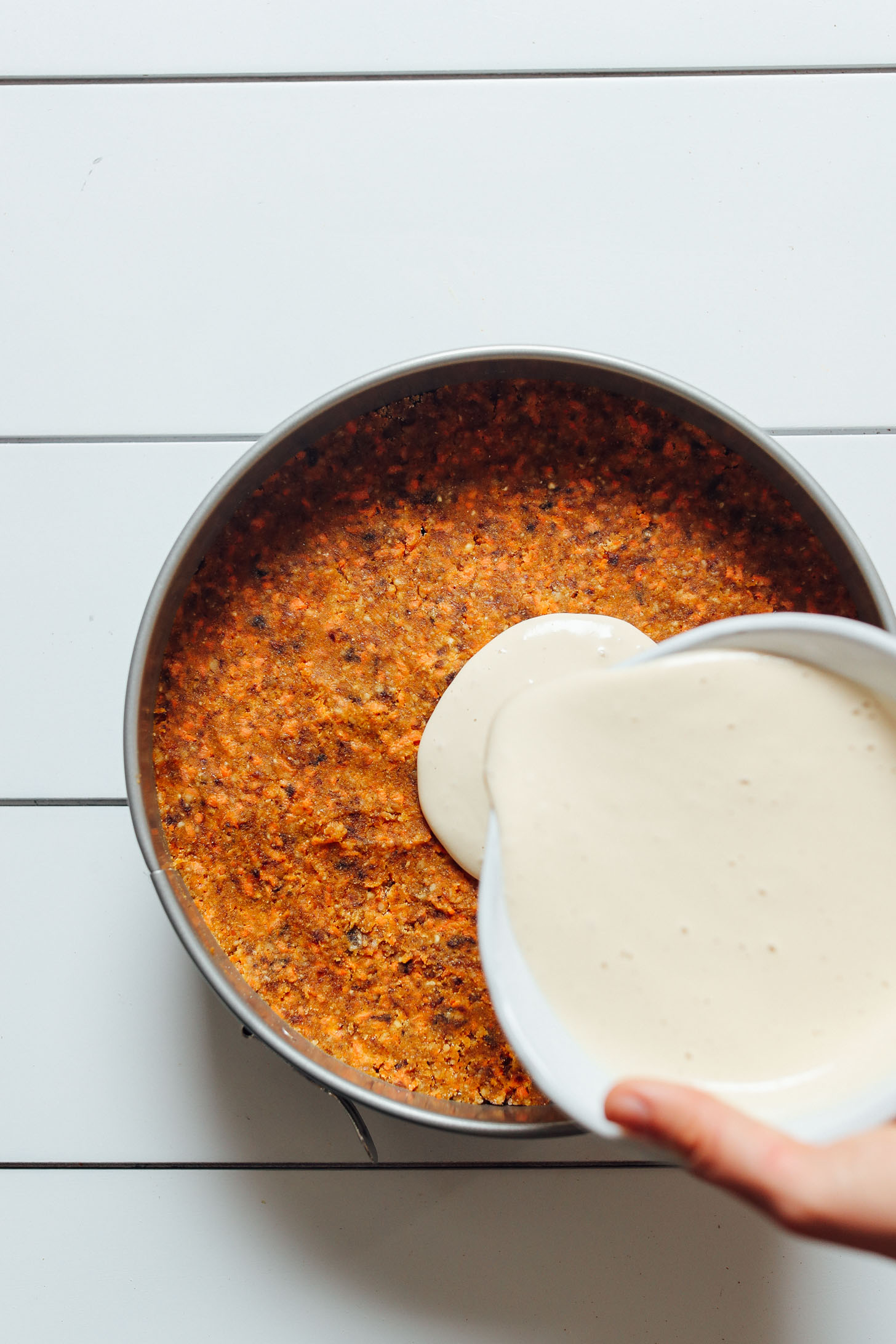 Pouring vegan cream cheese frosting over Raw Vegan Carrot Cake