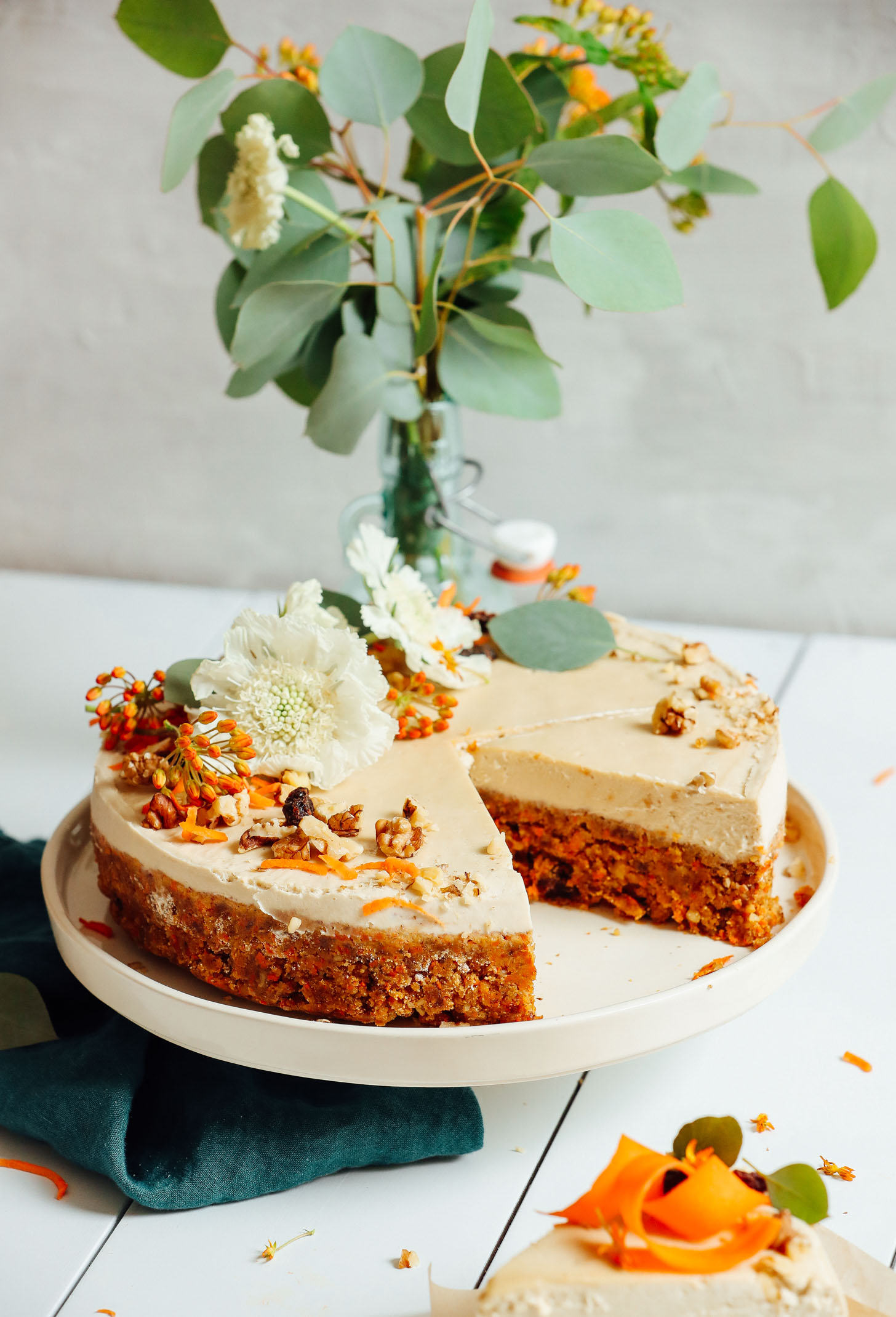 Raw Vegan Carrot Cake decorated with flowers, walnuts, shredded carrots, and raisins