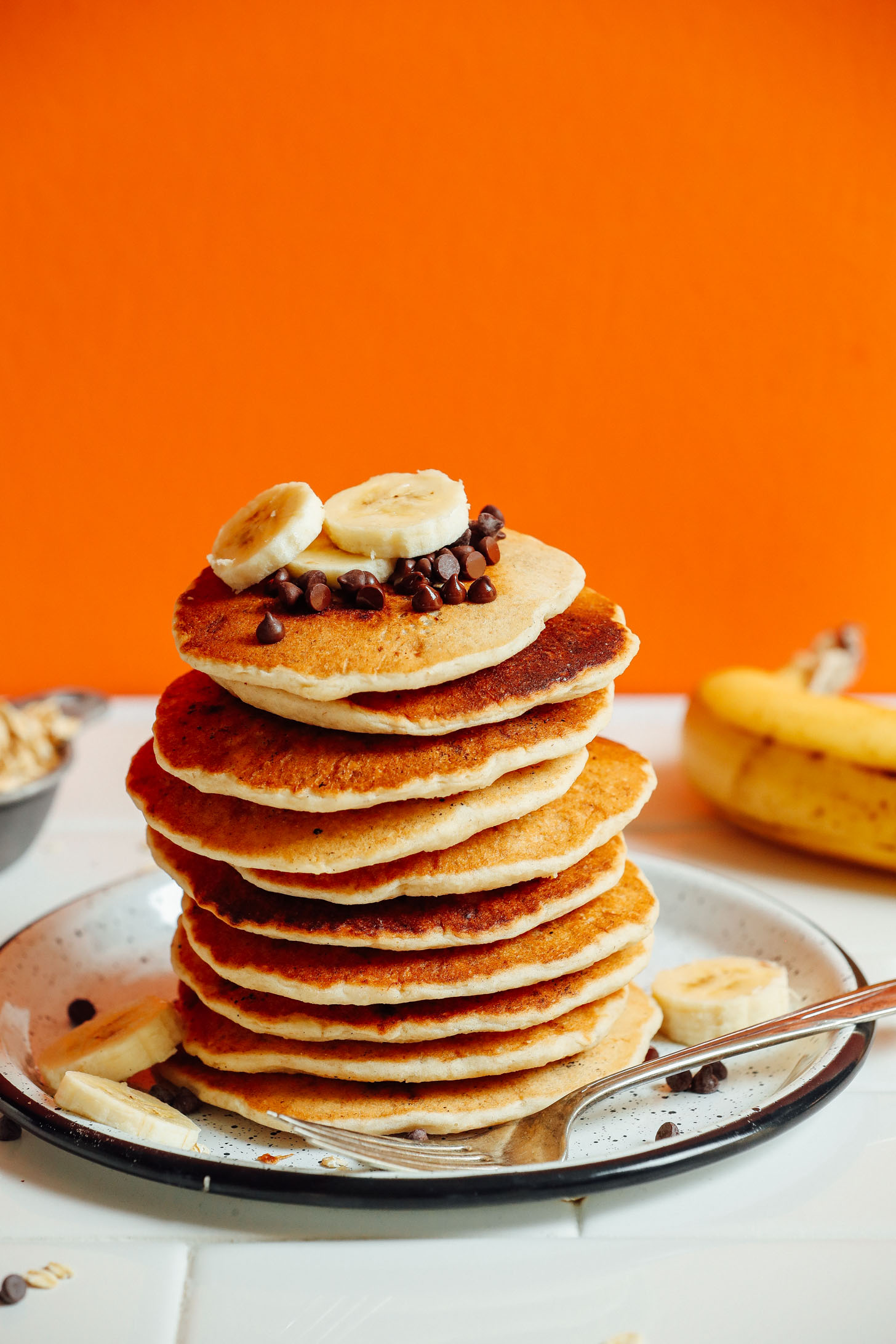 Plate of Banana Oat Pancakes topped with sliced banana and vegan chocolate chips