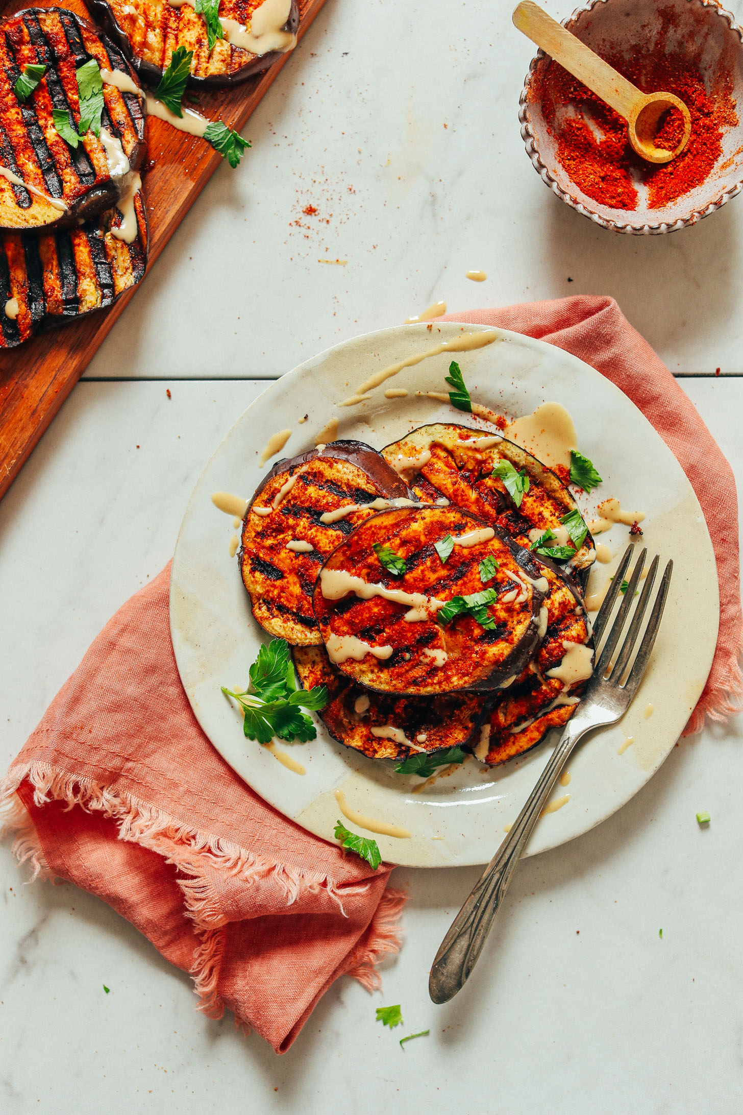 An overhead shot of simple grilled eggplant slices seasoned with smoky spice blend and drizzled with tahini and fresh parsley.