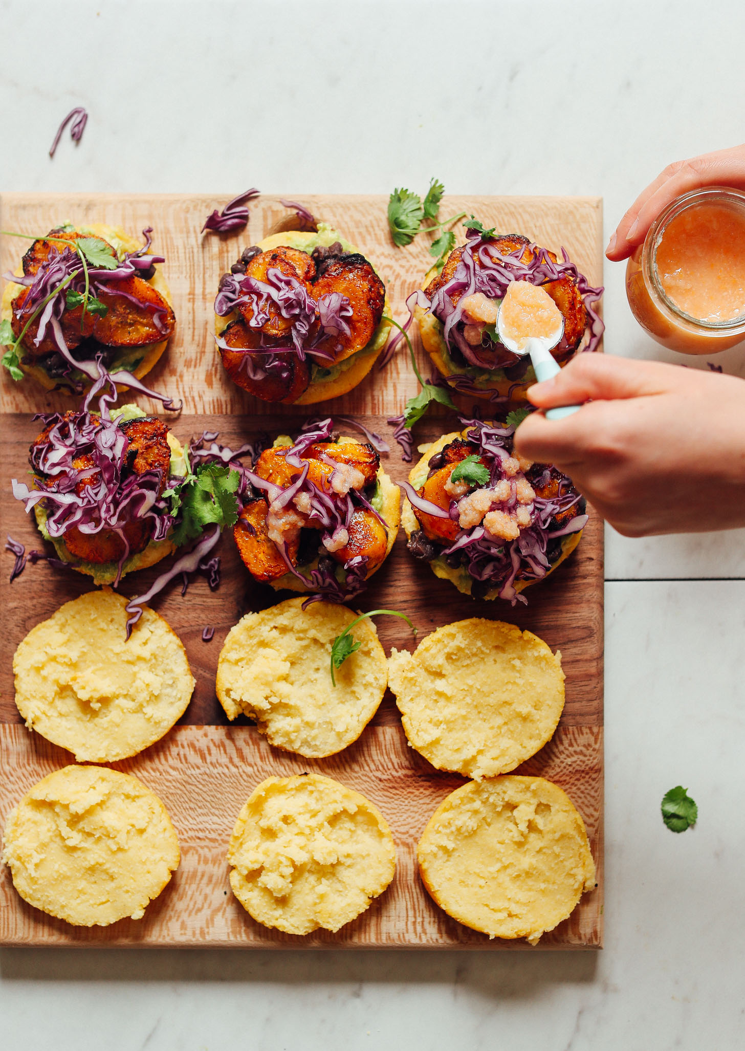 Using a spoon to add habanero hot sauce to gluten-free Vegan Arepa Sandwiches