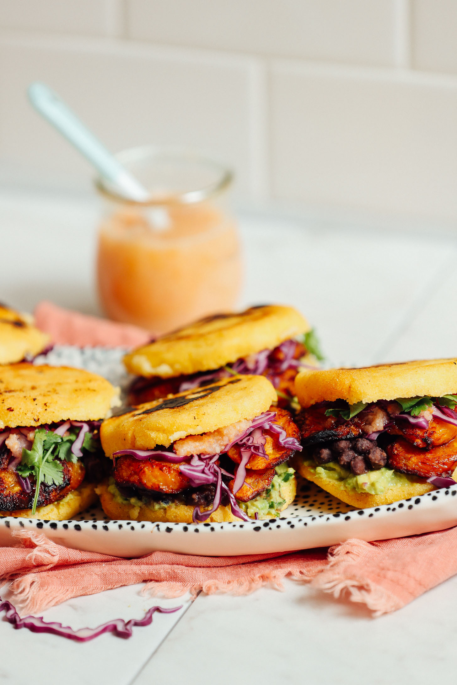 Tray of Vegan Arepa Sandwiches with Plantains, Black Beans, Guacamole, and a jar of habanero hot sauce
