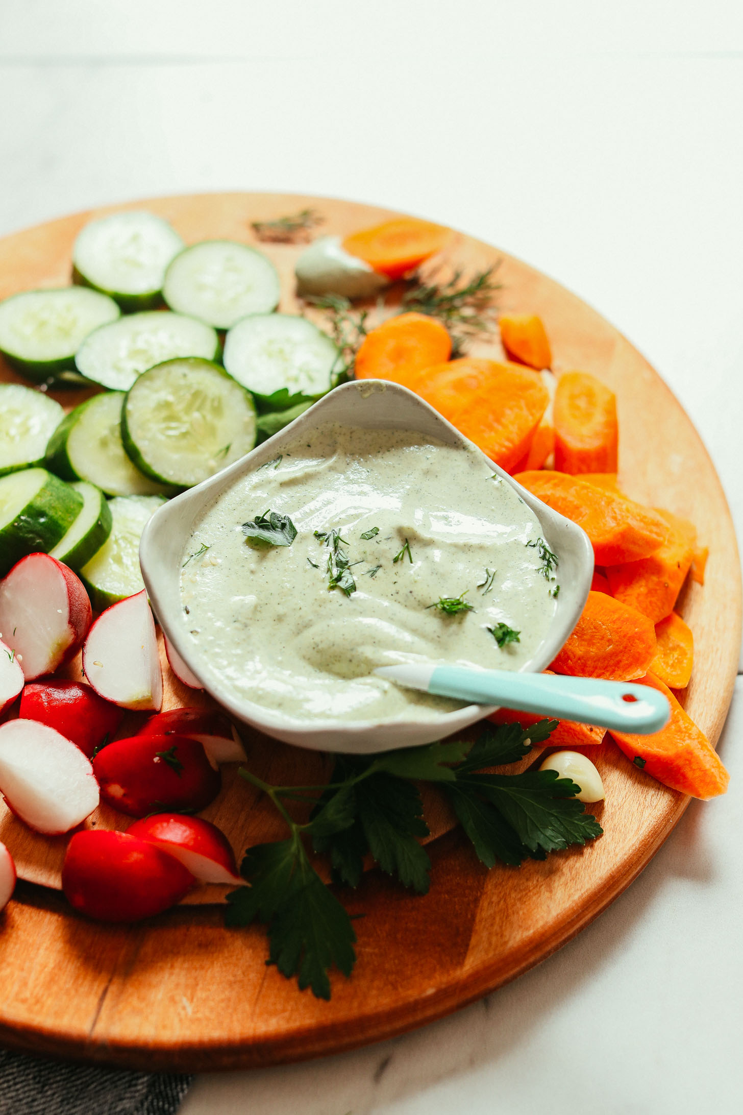 Close up shot of a wood cutting board filled with sliced veggies and homemade Vegan Ranch