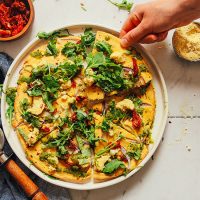 Grabbing a slice of gluten-free vegan Socca Pizza from a plate