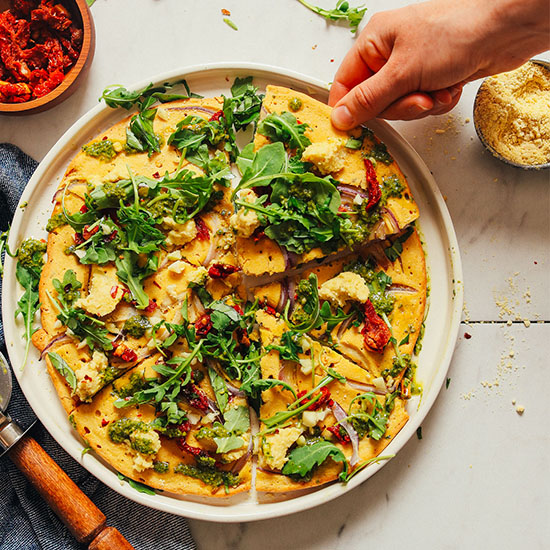 Grabbing a slice of gluten-free vegan Socca Pizza from a plate
