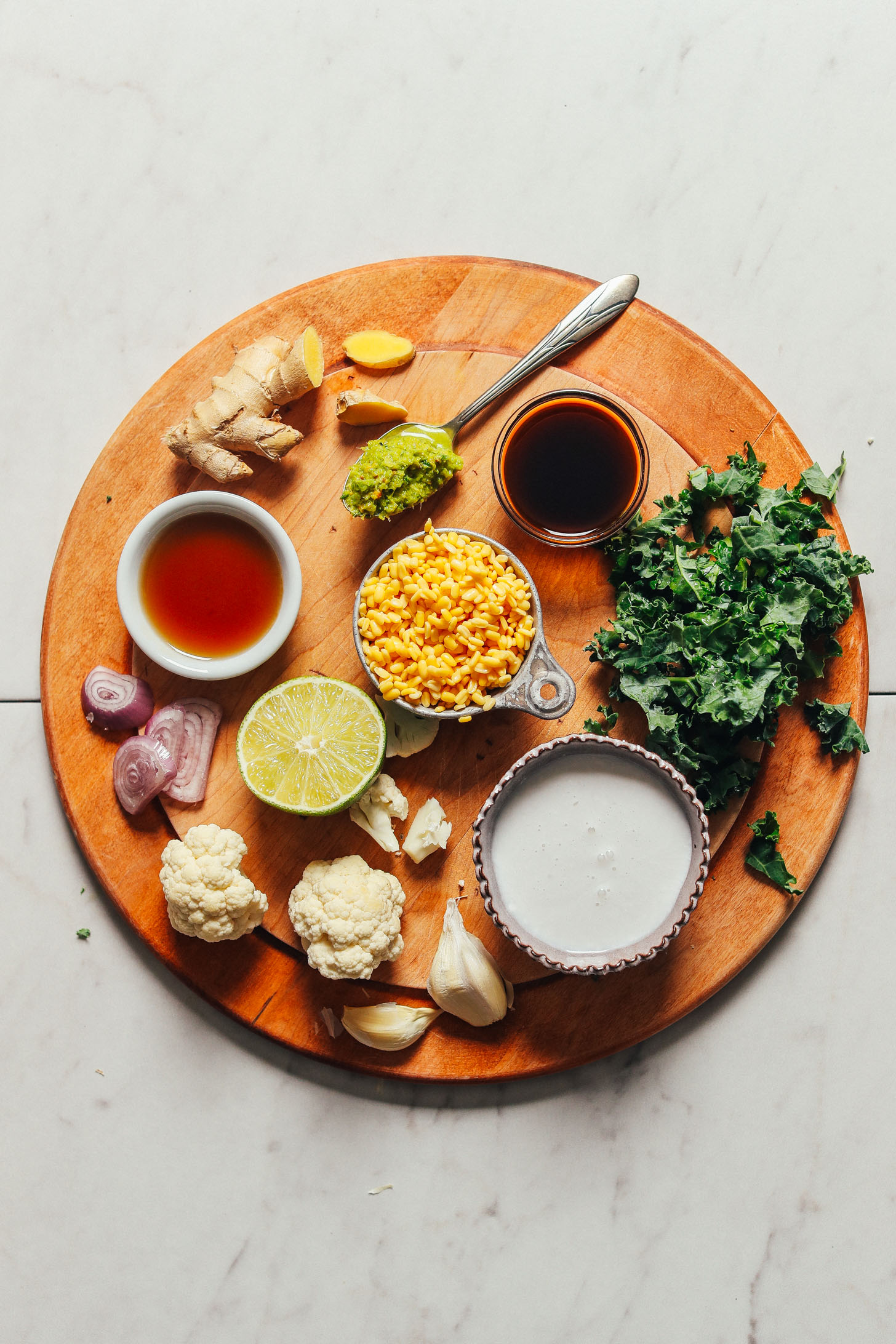 Overhead image of ingredients for a green dal curry on a cutting board including ginger lentils kale and lime