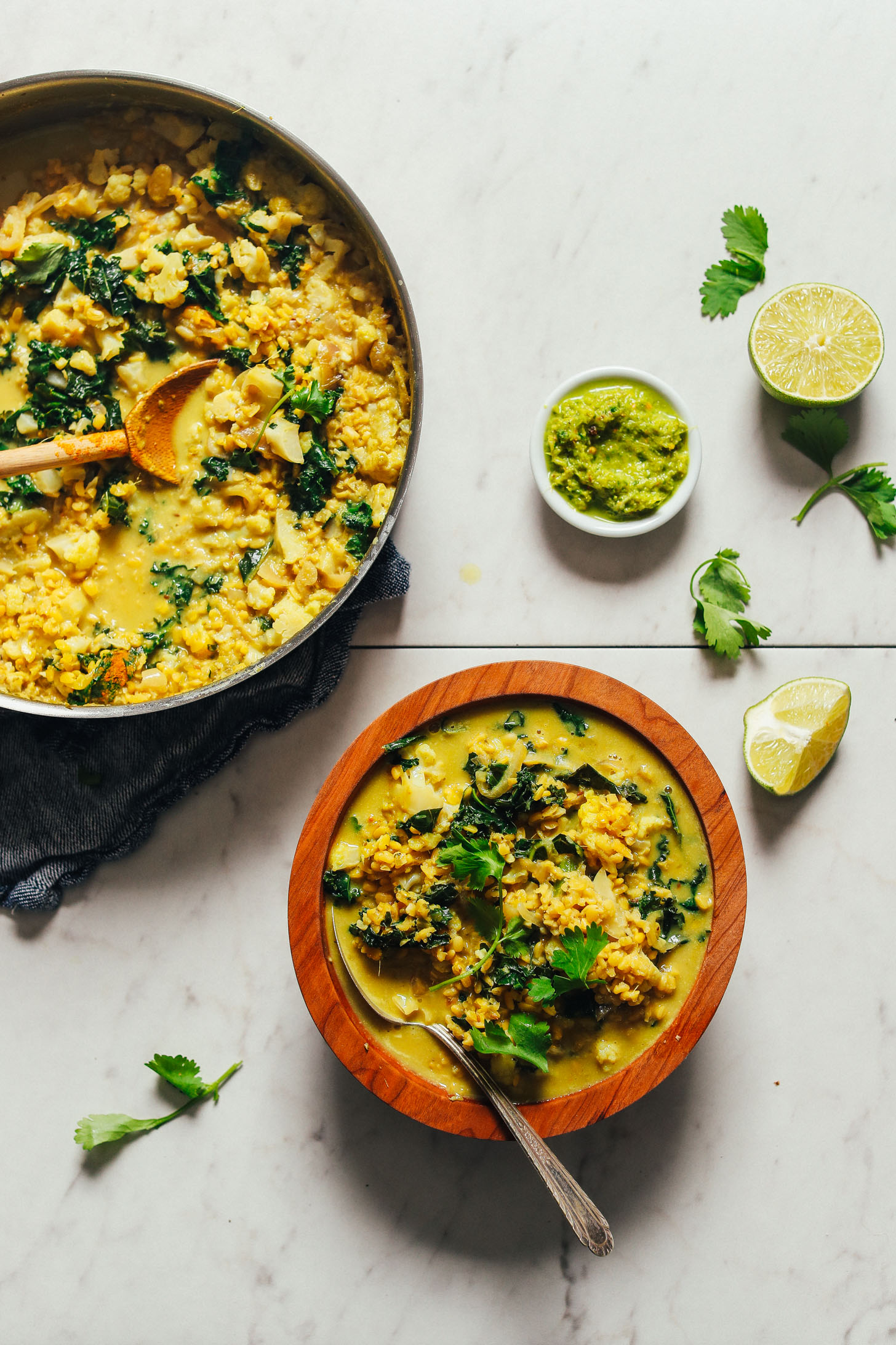 Overhead image of green curry with lentils served in a pot with a small wooden serving bowl and portion of the curry