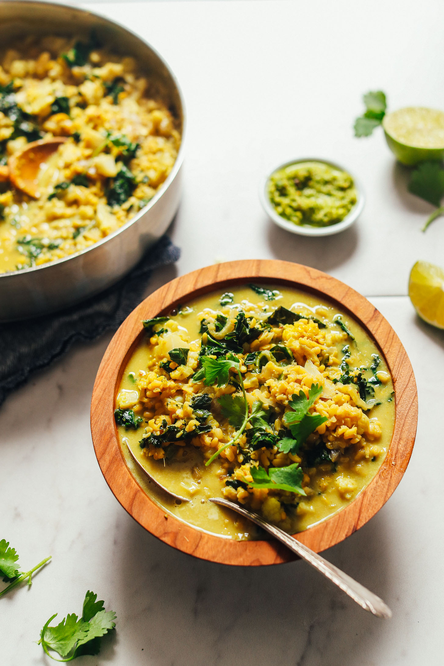 Image of green curry with kale and lentils in a wooden bowl with metal spoon