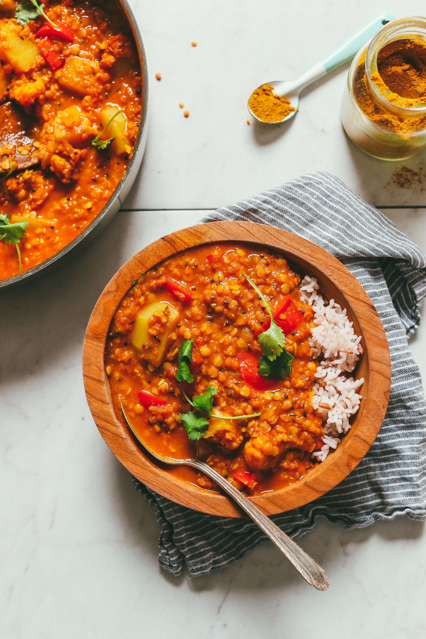 An overhead image with red lentil curry served in a wooden bowl with rice on the side and cilantro garnish