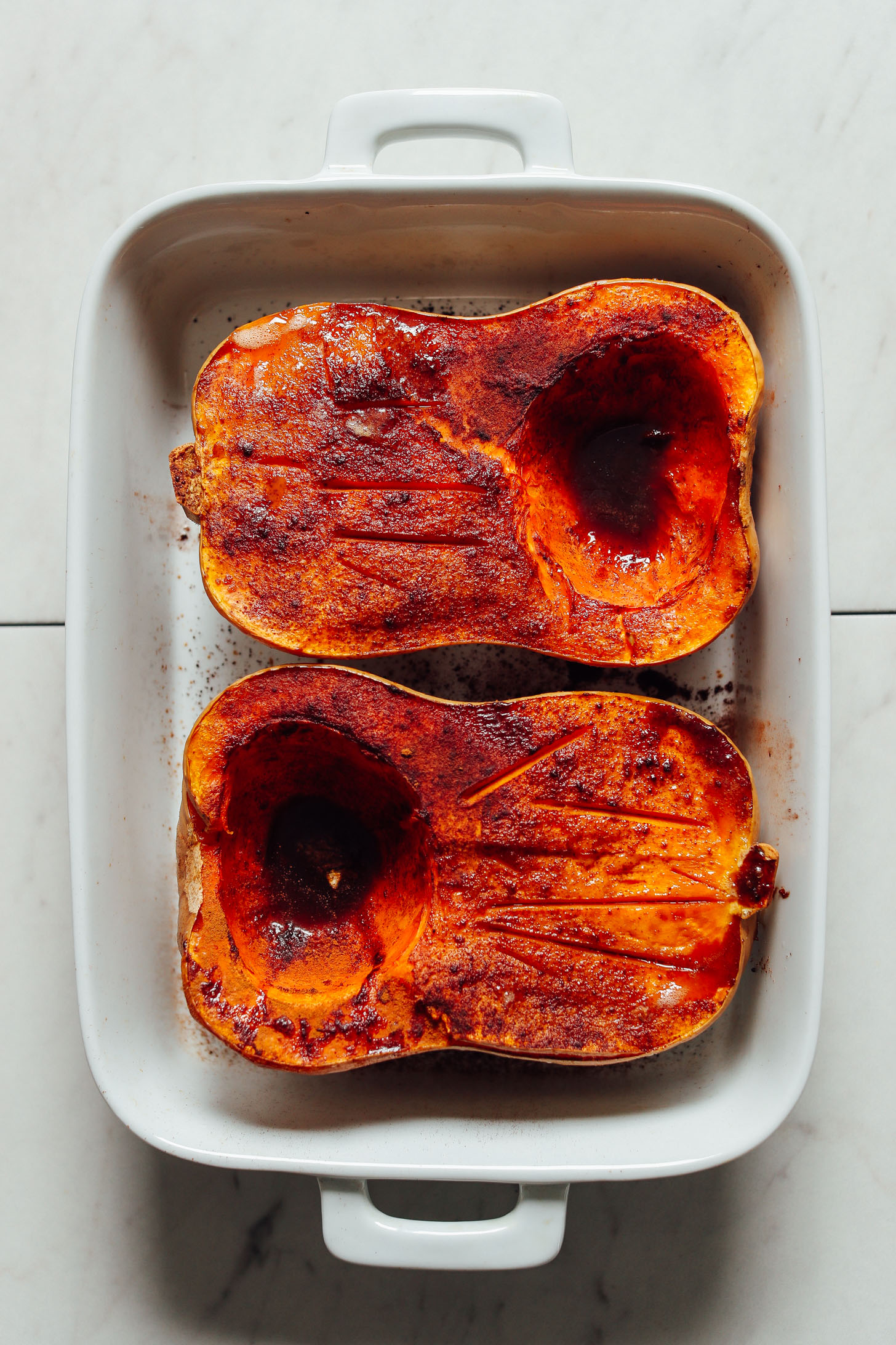 Baking dish with freshly baked halved butternut squash sprinkled with cinnamon