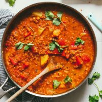 Wooden spoon in a pan of Cauliflower Potato Red Lentil Curry topped with fresh cilantro