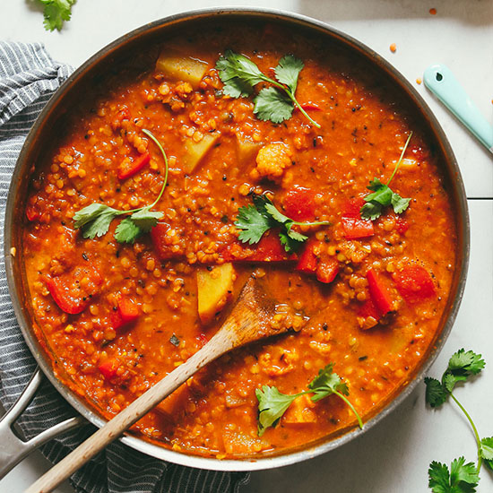 Wooden spoon in a pan of Cauliflower Potato Red Lentil Curry topped with fresh cilantro