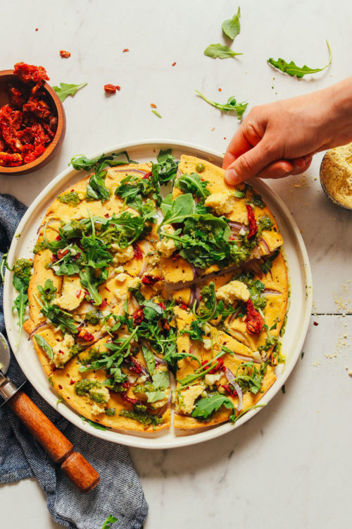 Grabbing a slice of gluten-free Socca Pizza made with Vegan Pesto