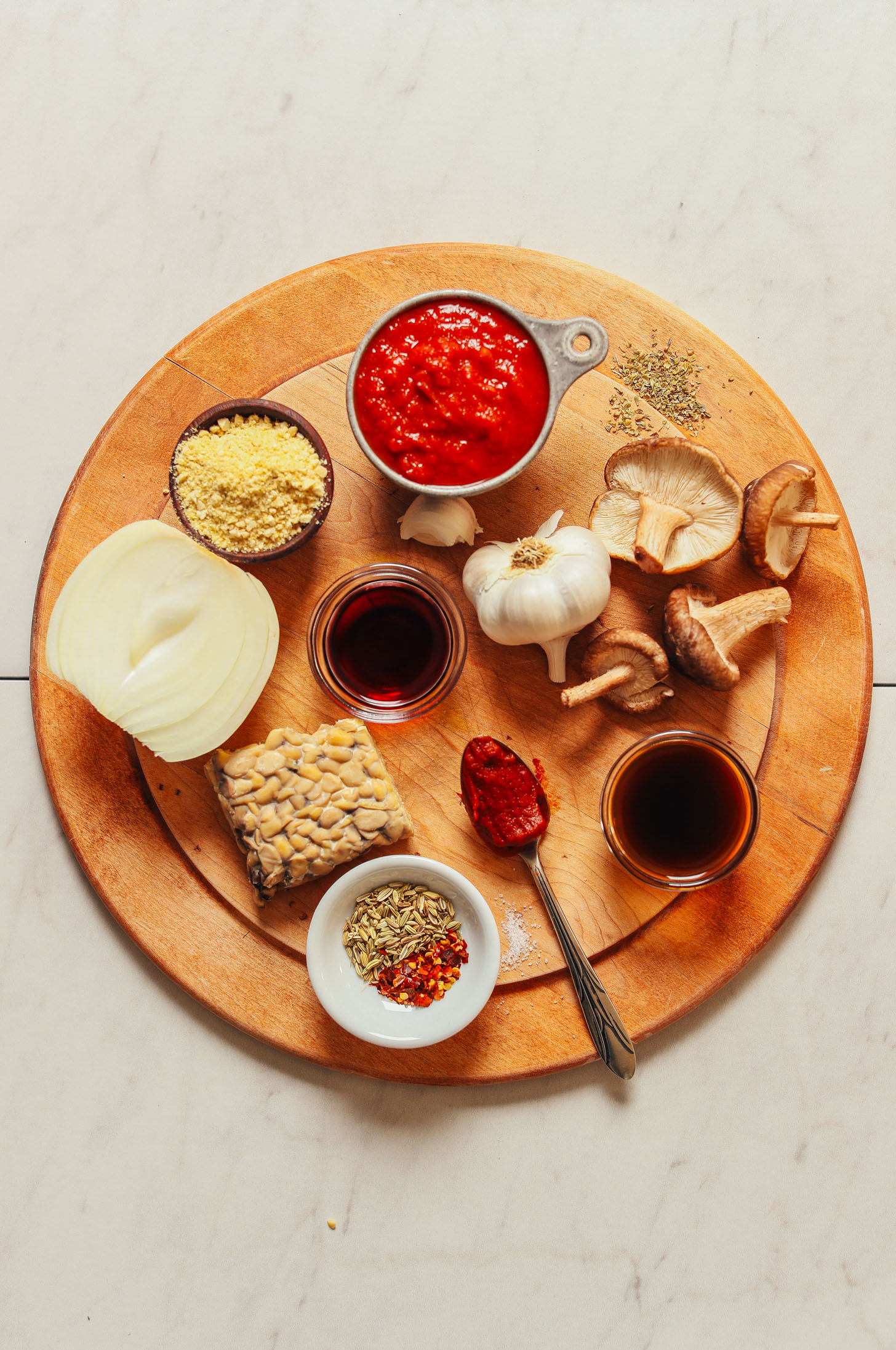 Overhead image of tempeh bolognese ingredients on a cutting board, including tempeh, onion, tomato sauce, and mushrooms