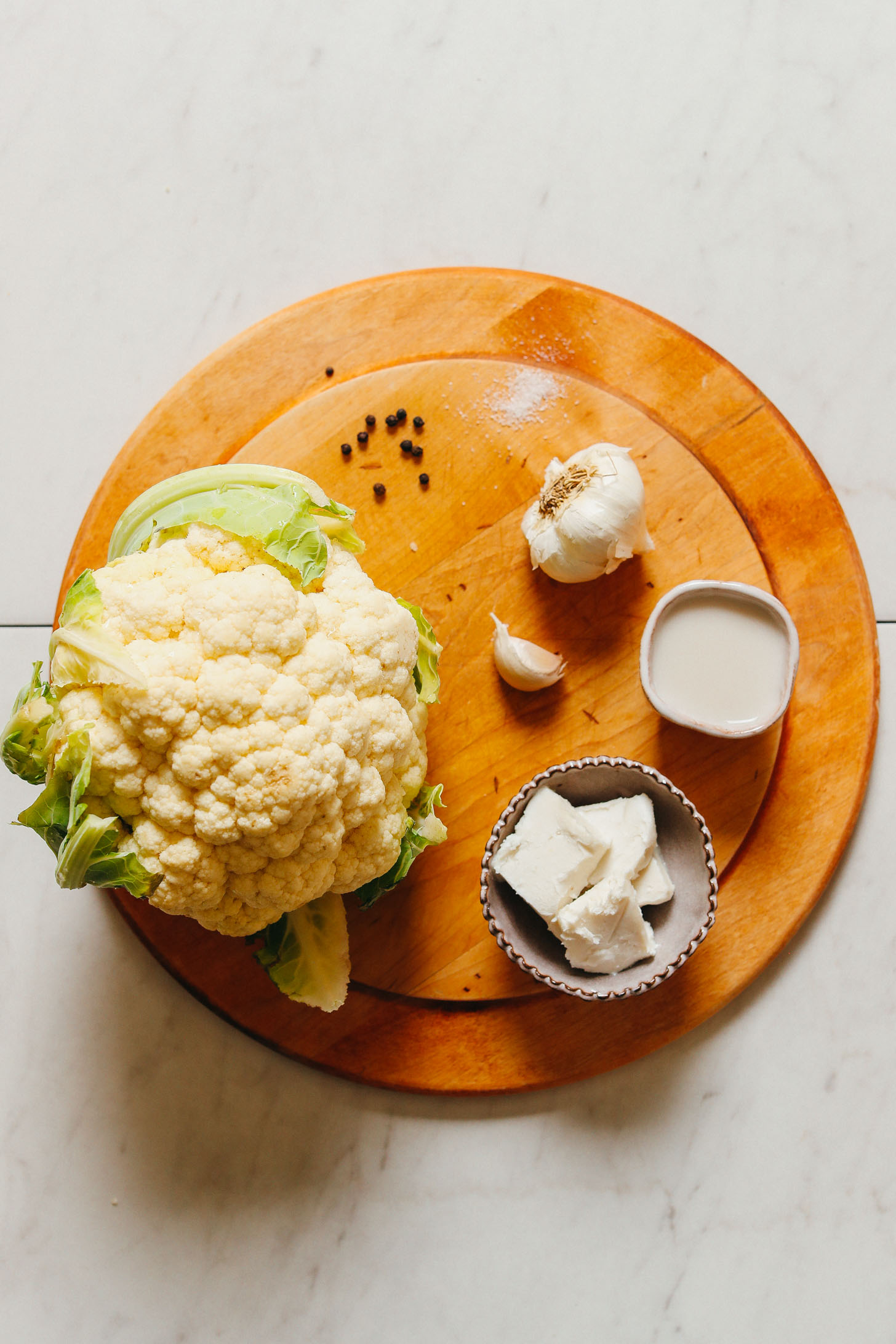 Cutting board with cauliflower, garlic, and other ingredients for making vegan Cauliflower Mashed "Potatoes"
