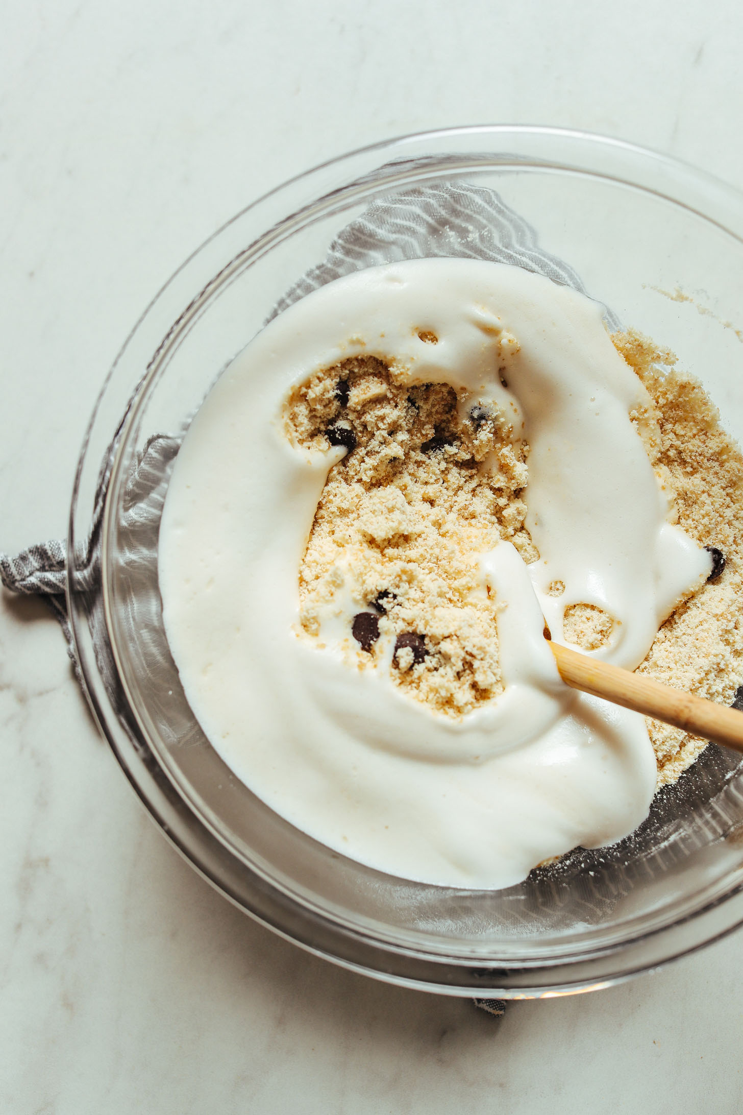 Using a wooden spoon to stir aquafaba into dry ingredients for vegan chocolate chip cookies