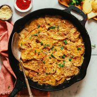 Cast-iron skillet of Vegan Scalloped Potatoes topped with chopped parsley