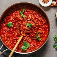 Wooden spoon in a pan of Vegan Tempeh Bolognese topped with fresh parsley leaves