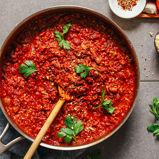 Wooden spoon in a pan of Vegan Tempeh Bolognese topped with fresh parsley leaves